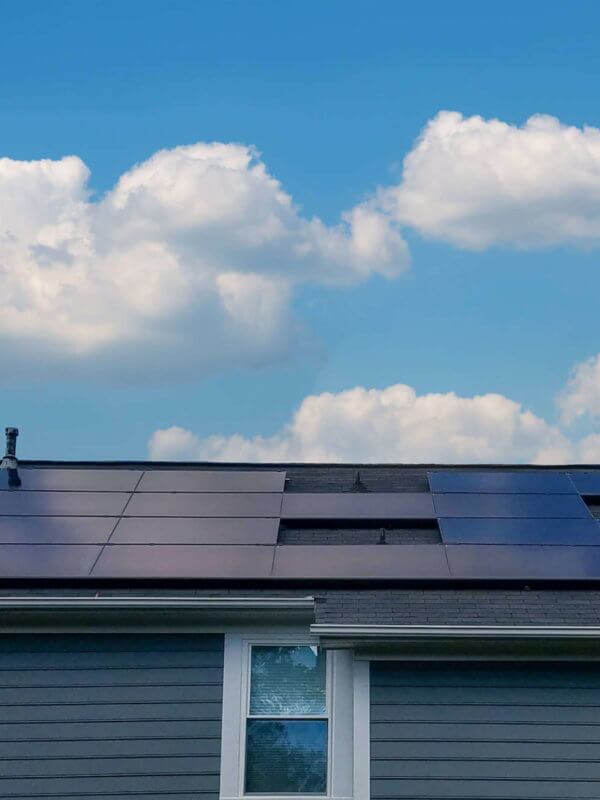Back view of a blue siding house with large solar panel system installed and bright blue sky above