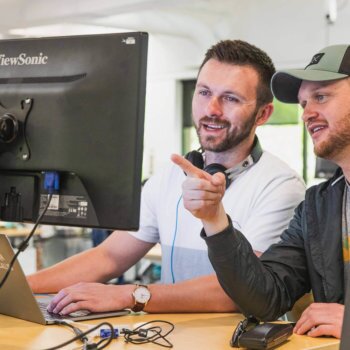 Two males working together while pointing and viewing a computer monitor