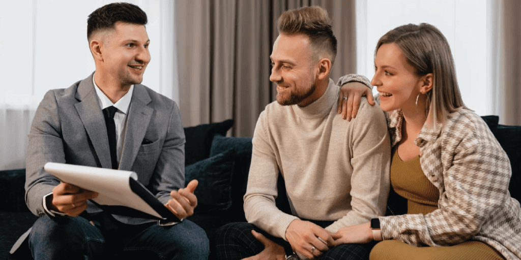 A business professional dressed male sitting with a happy couple, proposing a signature on paperwork