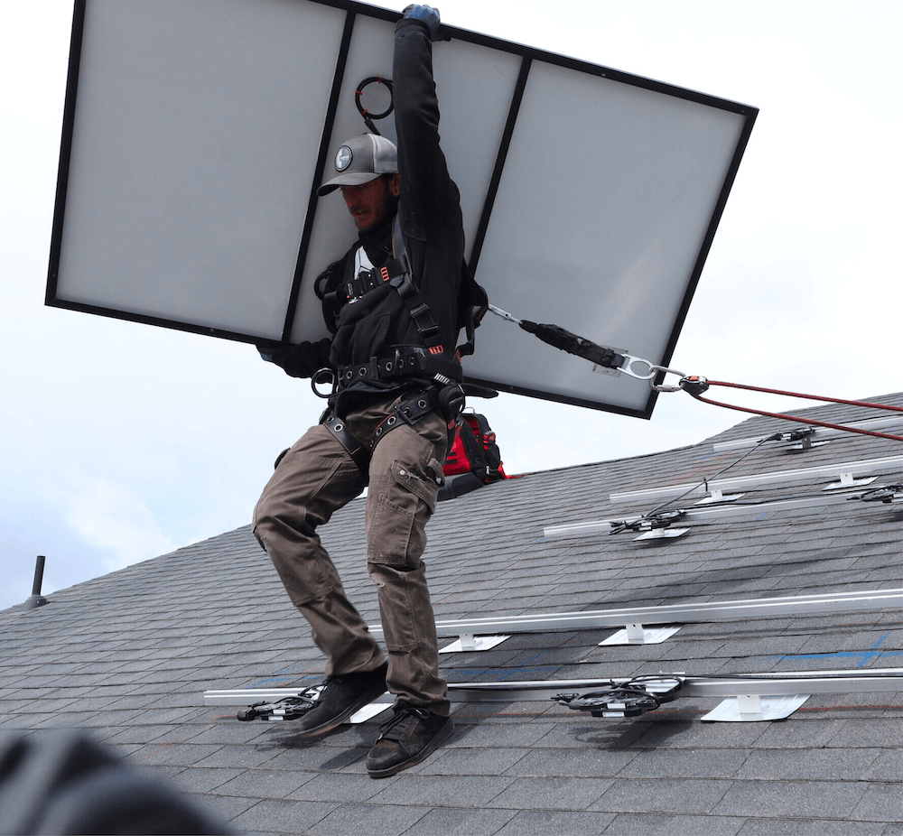 Blue Raven Solar Installer_Panel Male, Blue Raven Solar installer holding a PV panel above his head-on a roof during an installation