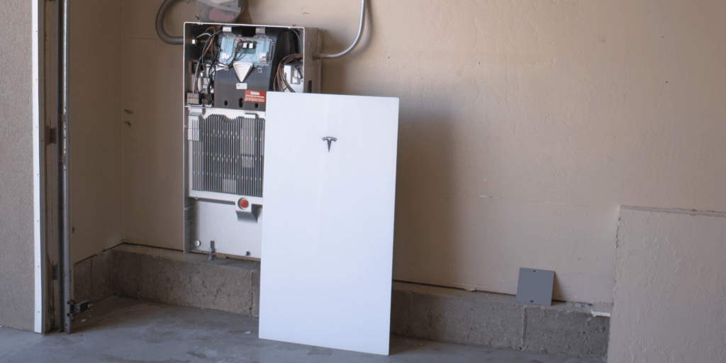 Tesla Powerwall solar battery installed in a garage, with the outer cover propped against it, revealing the inner workings and electrical components