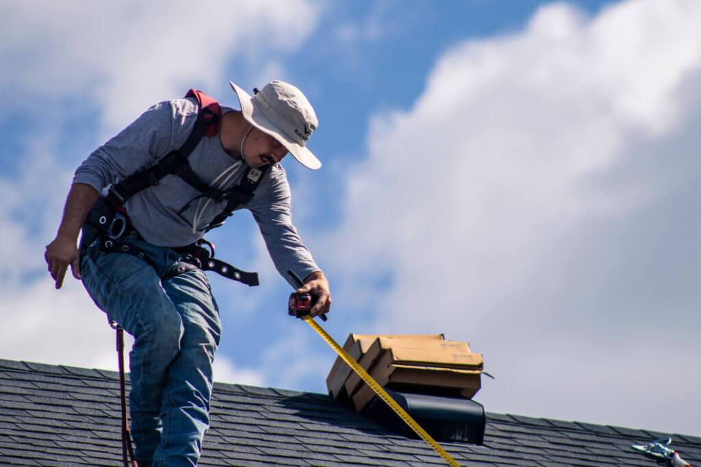Installer on roof with bucket hat and tape measure inspecting and mapping out the roof, prior to solar panel installation