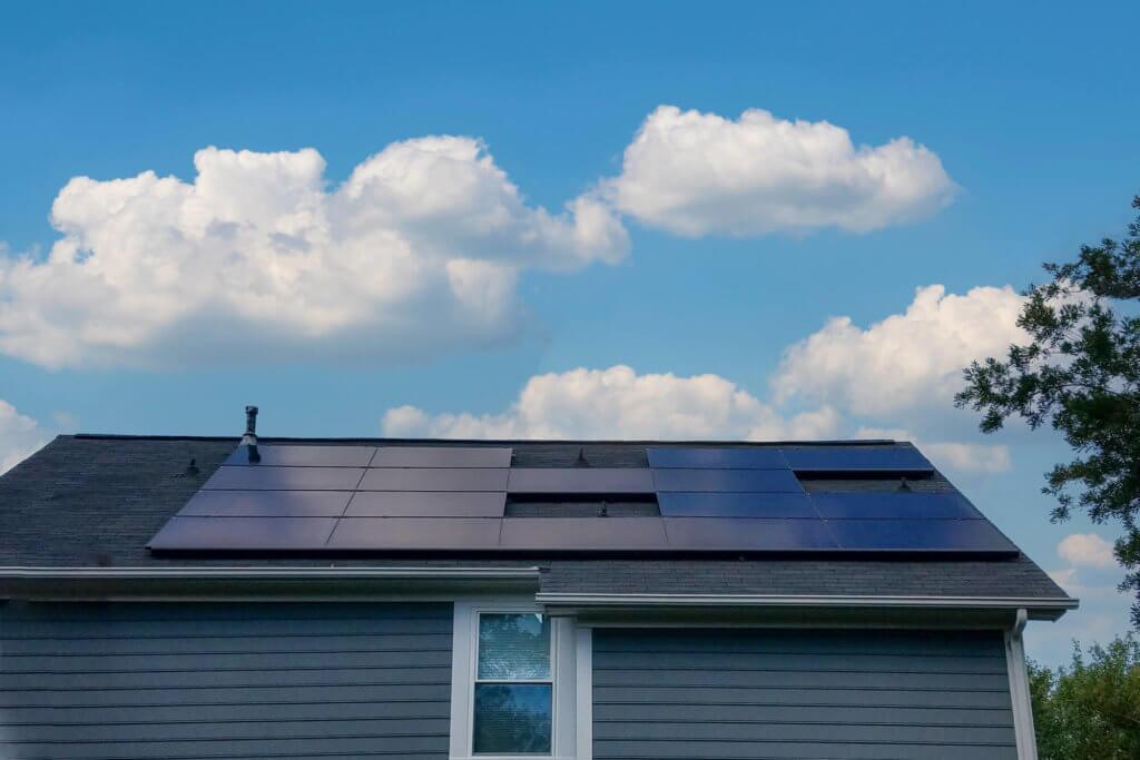Back view of a blue siding house with large solar panel system installed and bright blue sky above