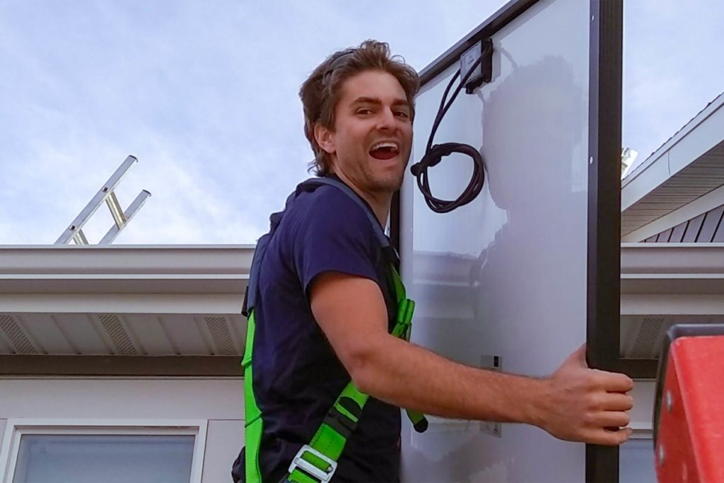 Ben Peterson, CEO of Blue Raven Solar, harnessed and holding a solar panel