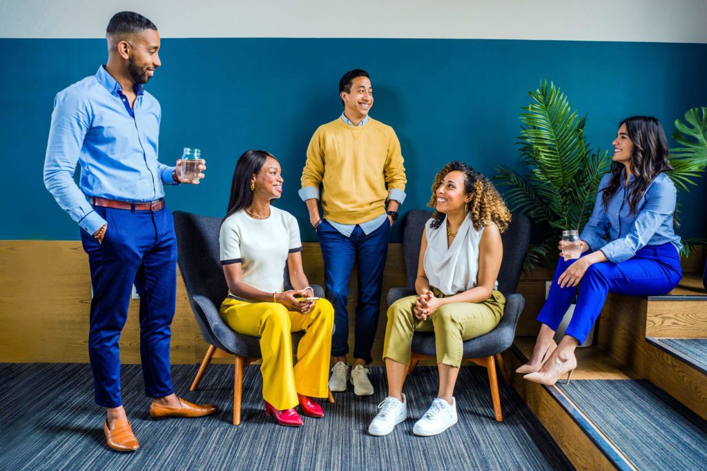 Group of five individuals standing and sitting, staged in a work environment
