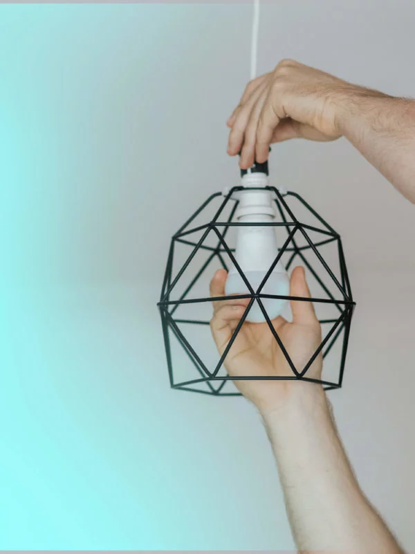 Human hands screwing in a light bulb into a modern ligh fixture with a turquoise and grey background