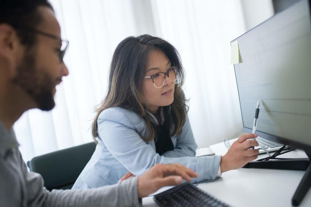 One male and one female, coworkers, evaluating data on a computer monitor