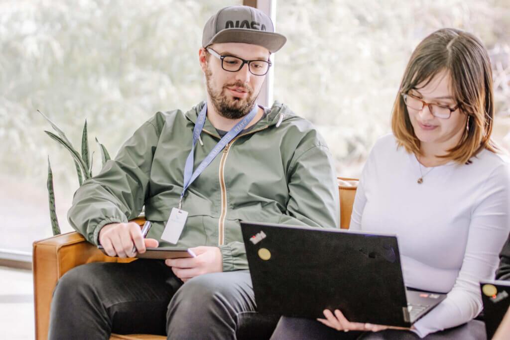 Two-Blue-Raven-Solar-Employees-in-the-Corporate-Lobby Two Blue Raven Solar employees, one male and one female, sitting next to each other on a couch in the corporate office lobby