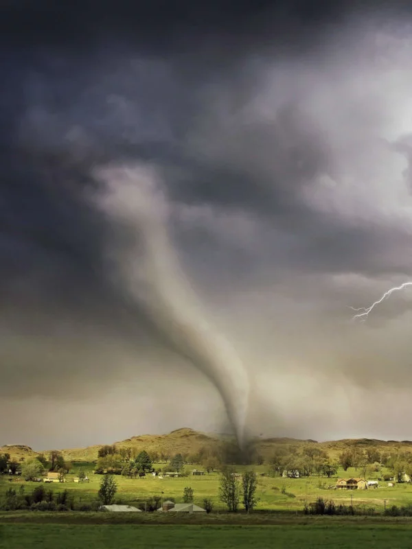 Dark clouds, tornado, and lightening striking a green hill scattered with houses and trees