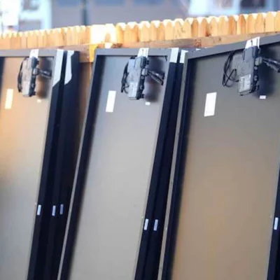 Back of solar panels, lined up against a wood fence