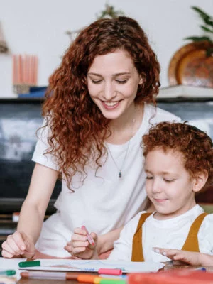 Mother-and-Son Red, curly haired female helping red-haired young child draw and color with markers