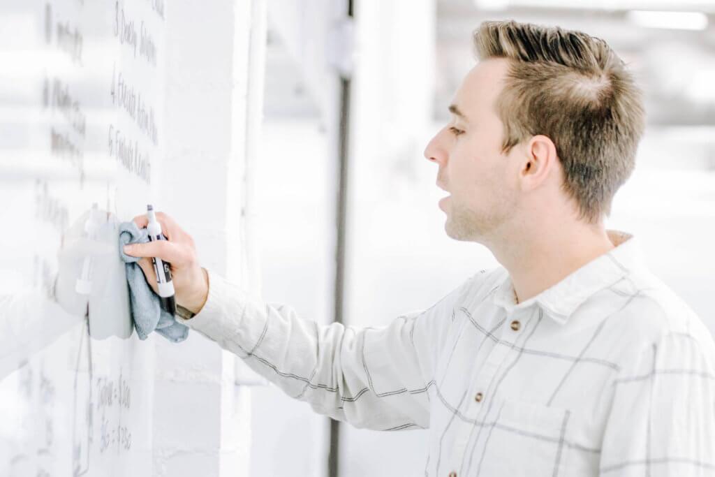 Young male in a while windowpane, collared, button-up shirt writing on a white board