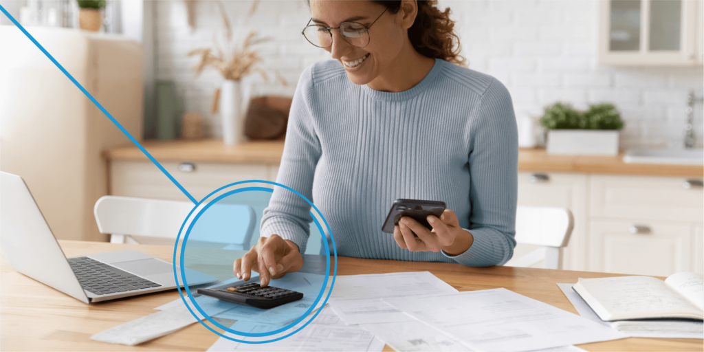 How the Solar Investment Tax Credit Works-01 Female sitting at a desk, in a light blue sweater, holding a smart phone while configuring calculations on a calculator