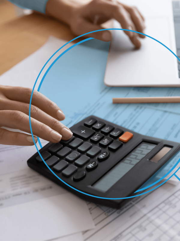 Individual working on a black calculator, sitting on top of paperwork, and laptop