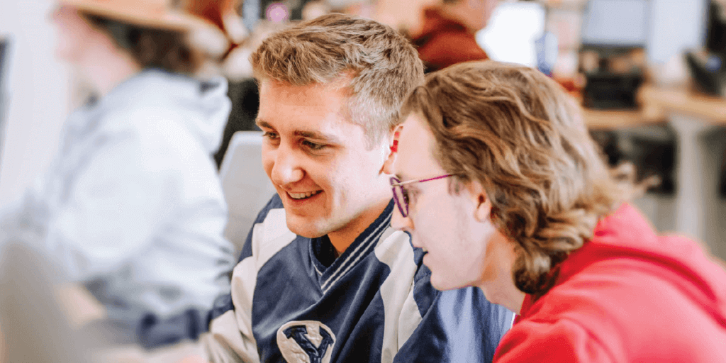 Two young males, looking at a computer screen in a corporate setting