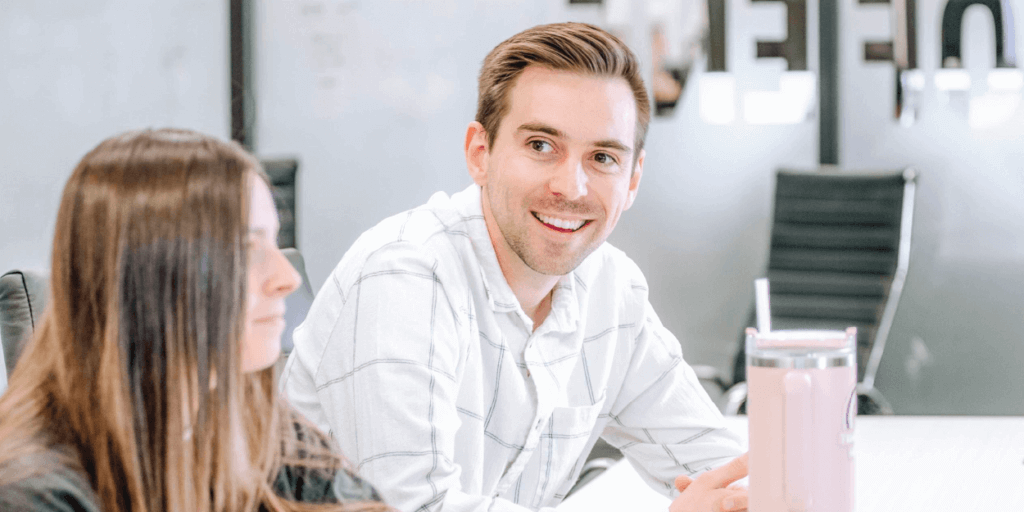 A young woman and young man, sitting at a conference table during a meeting