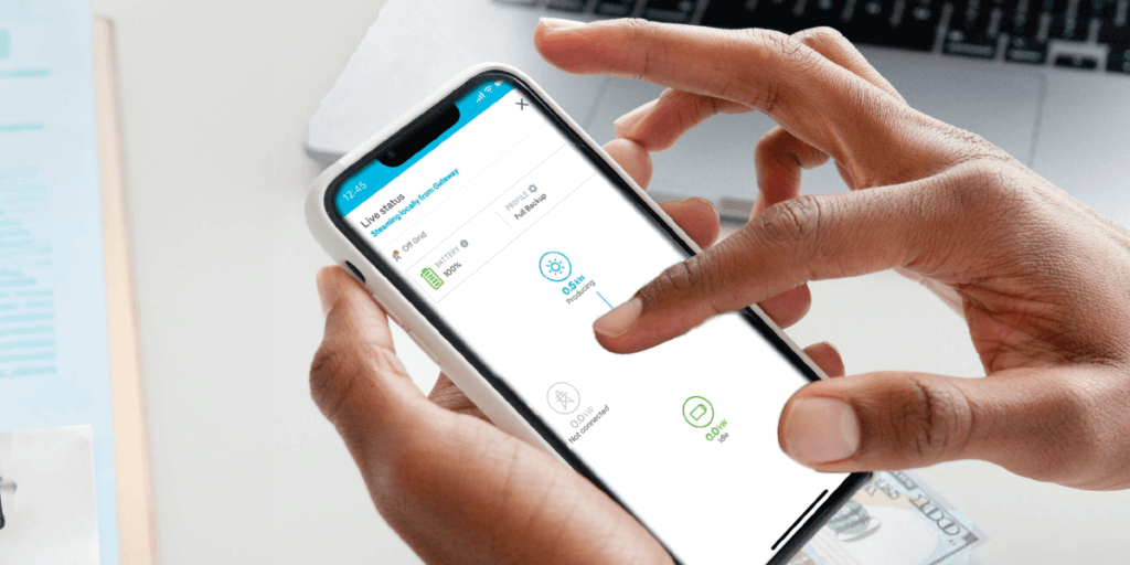 Mobile device held between two hands, scrolling with cash and a laptop in the background