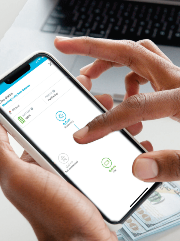 Mobile device held between two hands, scrolling with cash and a laptop in the background