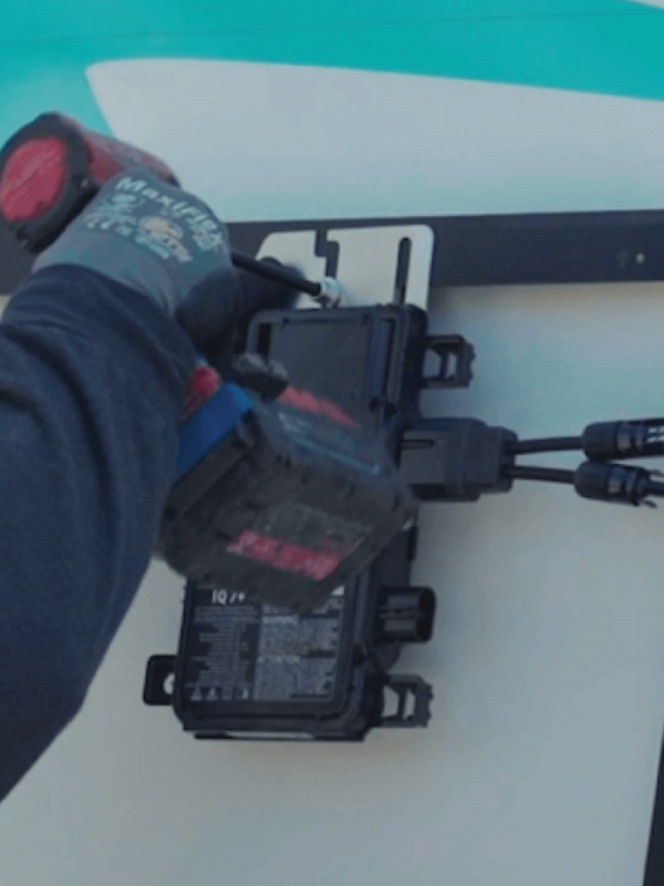 Solar expert securing a microinverter to the back of a panel using power tools
