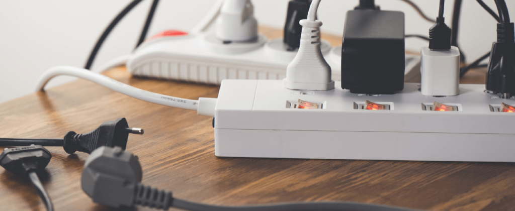 Multiple power strips with numerous products plugged-in sitting on a wood table