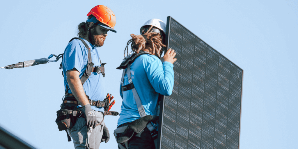 Two Blue Raven Solar installers placing a monocrystalline solar panel on a rooftop