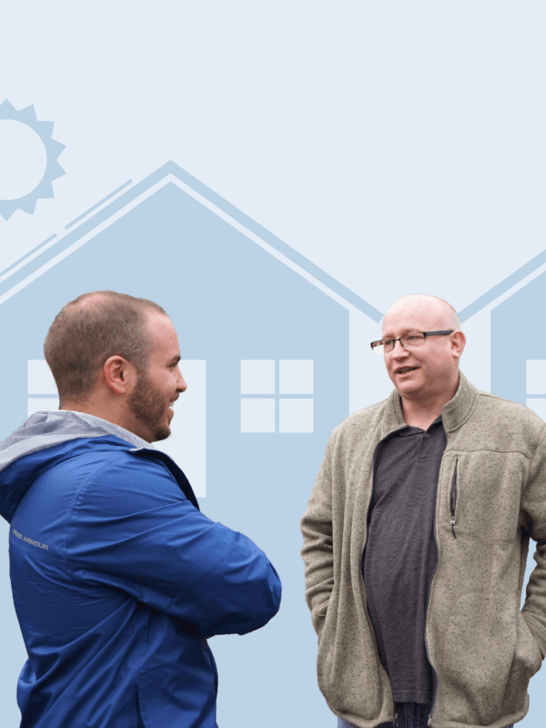 Two males standing and talking in front of two house graphics