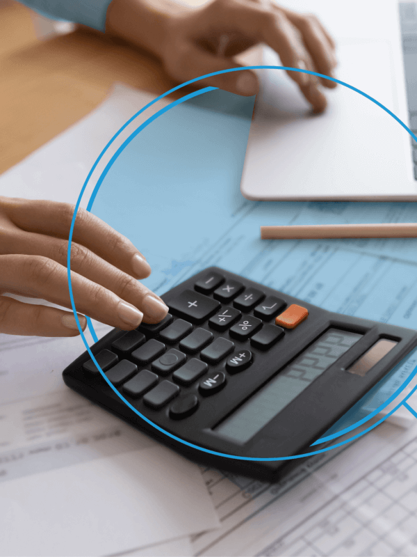 Individual working on a black calculator, sitting on top of paperwork, and laptop