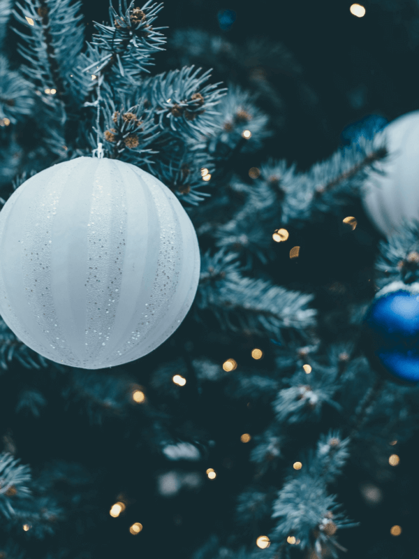 White and royal blue round holiday ornaments on a faux tree with golden lights in the background