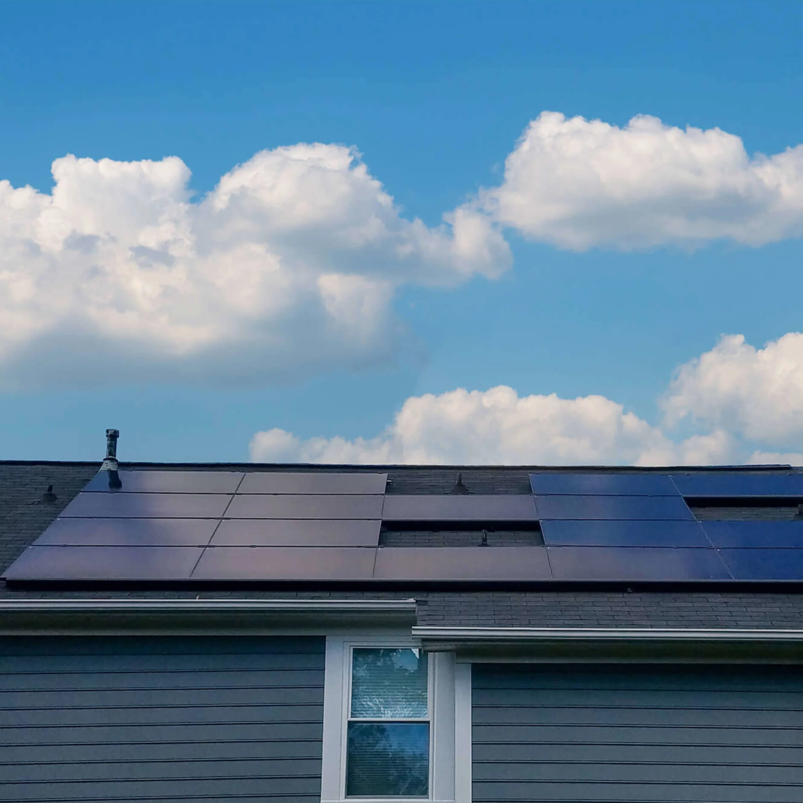 Back view of a blue siding house with large solar panel system installed and bright blue sky above
