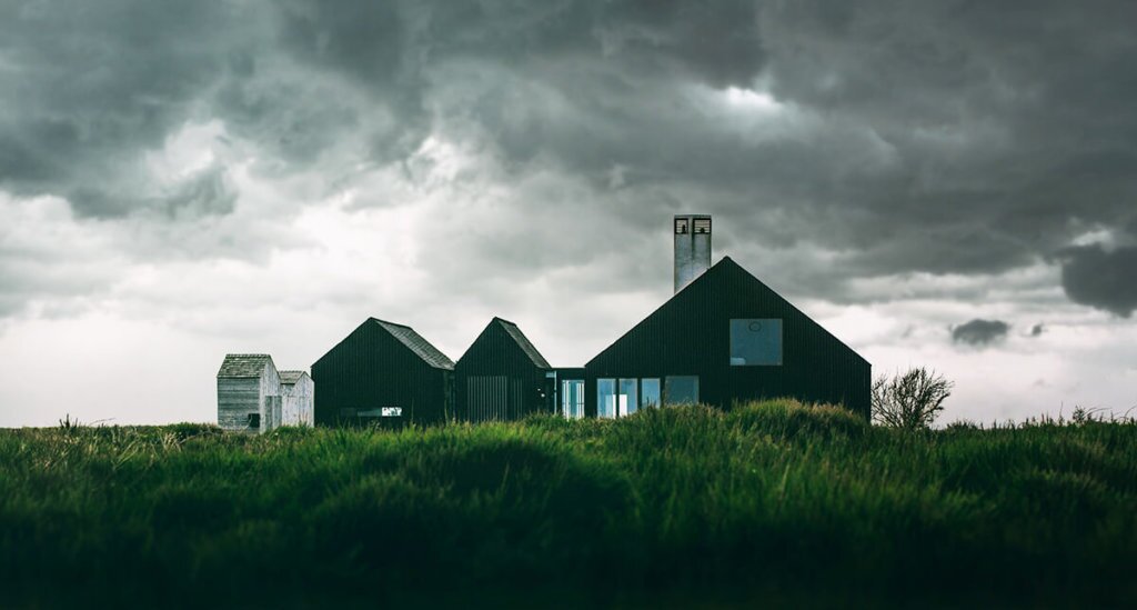 Cloudy Day Minmal black house surrounded by tall green grass and dark rain clouds in the background