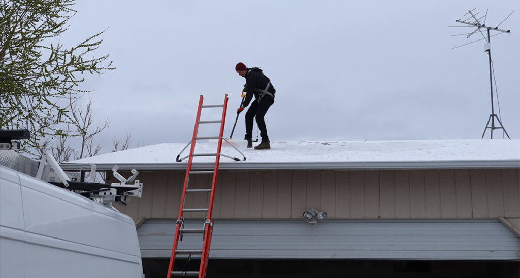 Snow Male standing on roof with professional cleaning tools, clearing off snow and debris