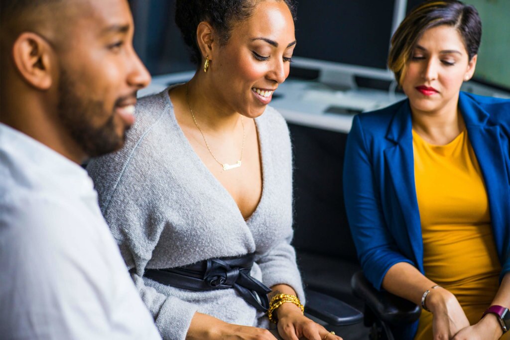 Three individuals working together on one laptop, probably attending a meeting and taking notes