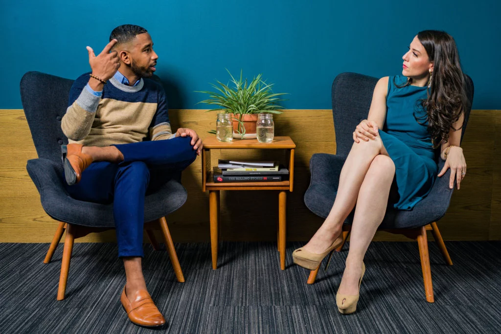 Two individuals, one male and one female sitting and looking at each other in deep conversation