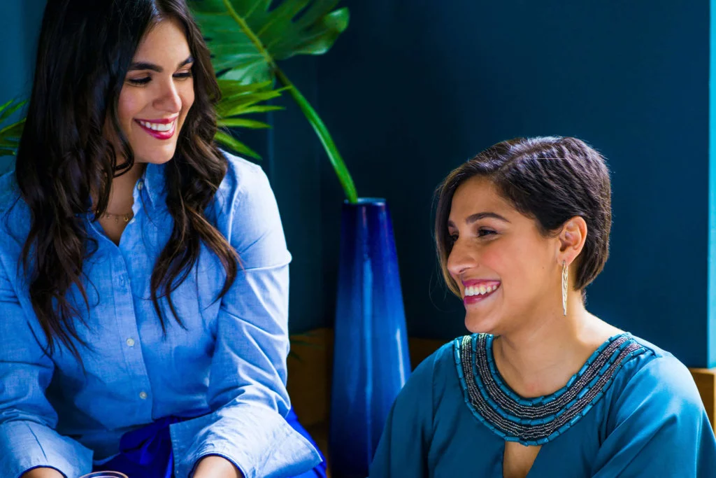 Two women in different blue tones and attires smiling