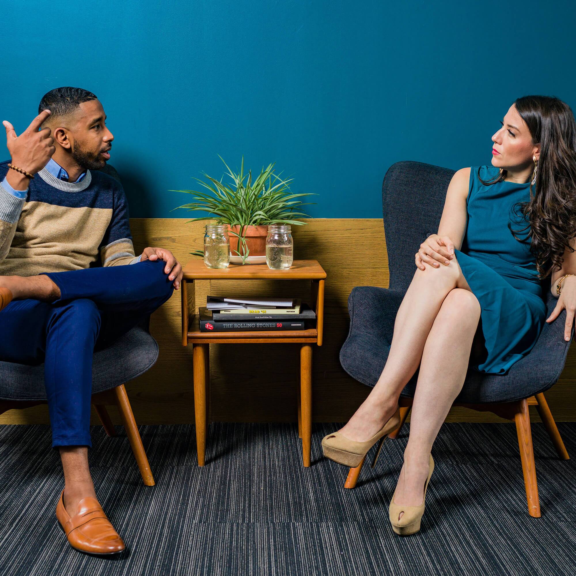 Two individuals, one male and one female sitting and looking at each other in deep conversation