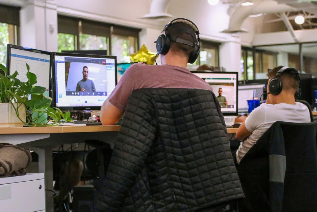Two-Blue-Raven-Solar-Employees-during-Video-Training Two male employees with headphones, watching training videos in an office setting