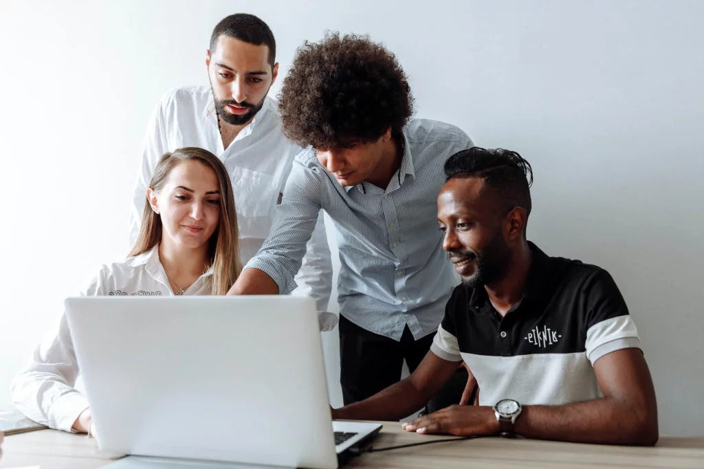 Group-of-People-working-on-a-laptop Three males and one female, gathered around a laptop - working in a group setting
