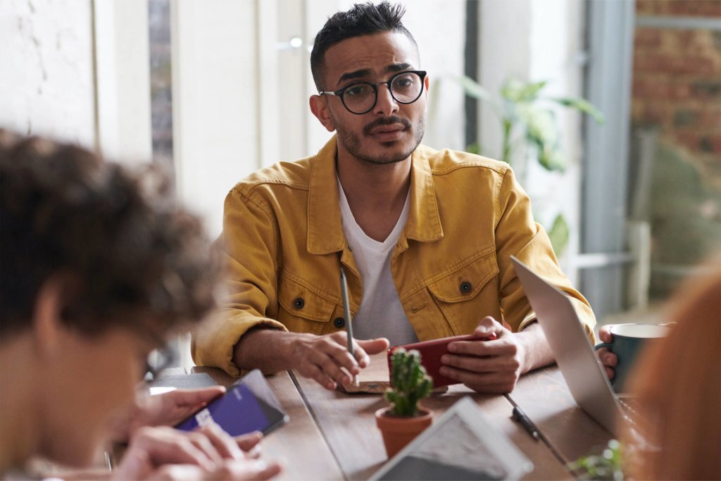 Male with glasses in a mustard colored jacket conducting a meeting