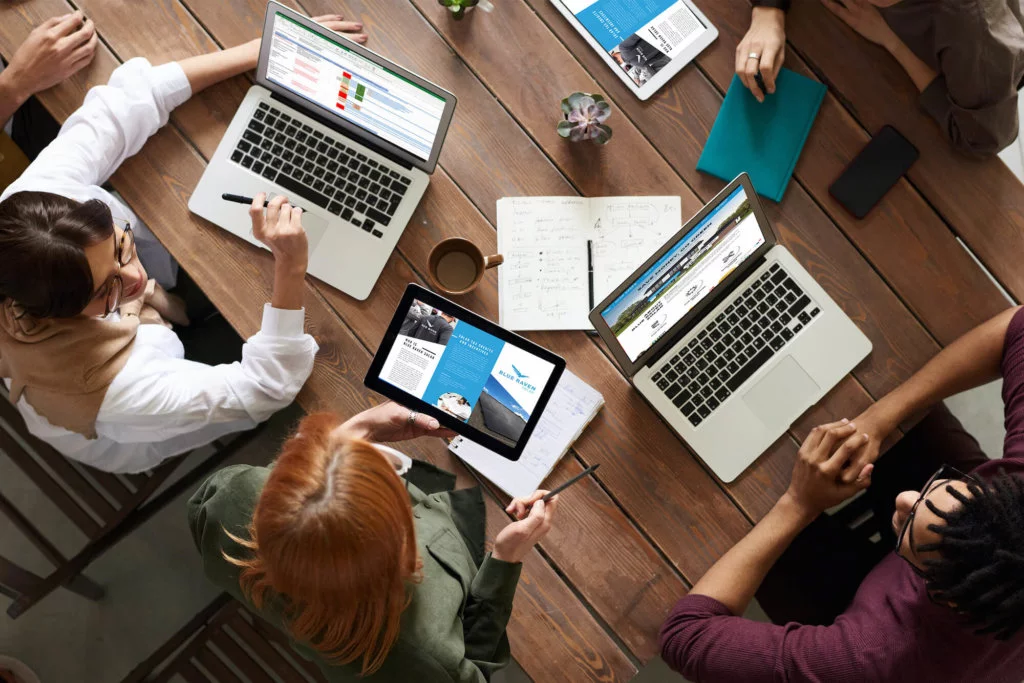 Three co-workers in a meeting working on laptops and iPads, collaborating