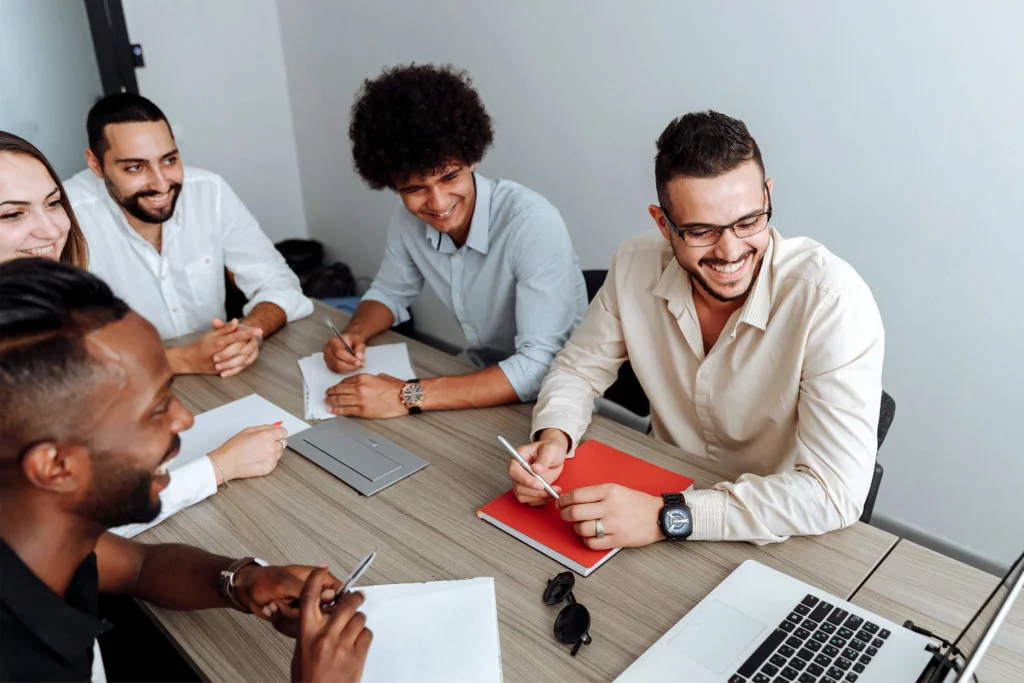 Team-of-Employees-in-a-Meeting Team meeting in a conference room, all participants looking at a laptop at the head of the table