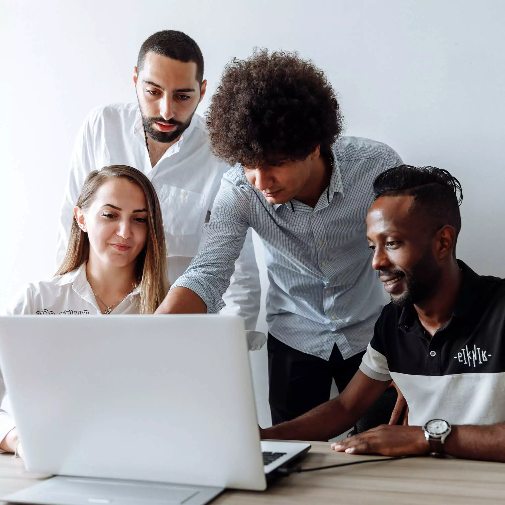 Three males and one female, gathered around a laptop - working in a group setting