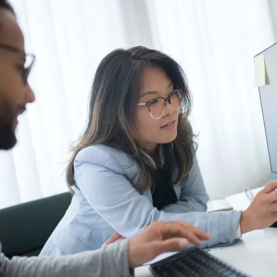 One male and one female, coworkers, evaluating data on a computer monitor