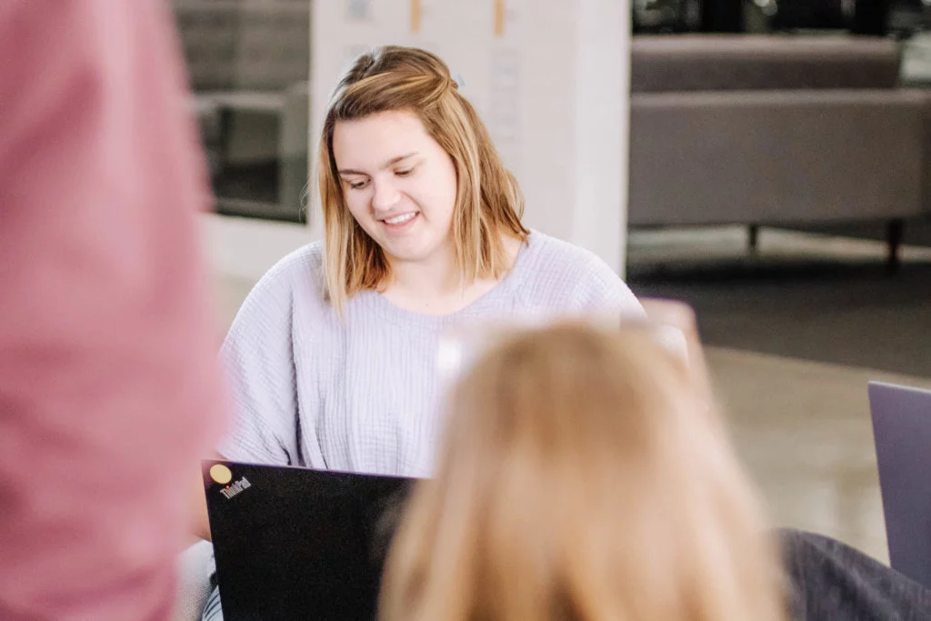 Blue-Raven-Solar-Employee-Working-in-a-Team Female with shoulder length hair, working on a laptop and collaborating with a team of people