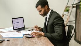 Tax-Incentives Black male in a suit, sitting at a desk filing tax documents and other paperwork