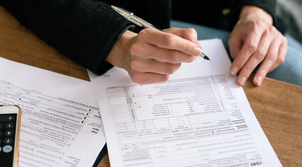 Taxes and Paperwork An individual filing tax paper and paperwork on a deak, using their phone as a calculator