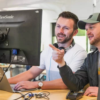 Two males working together while pointing and viewing a computer monitor
