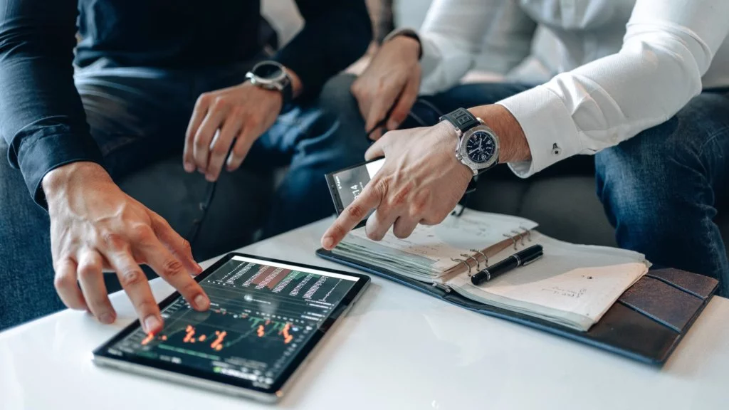 Two males sitting and discussing data on a tablet and taking notes