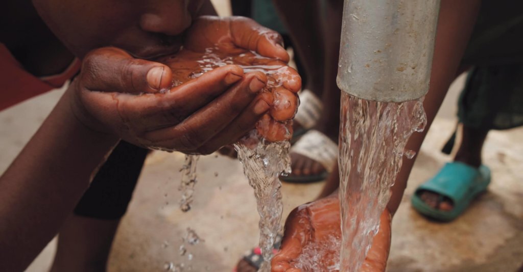 Child Drinking Clean Water Small black child drinking clean water from hands out of a silver pipe