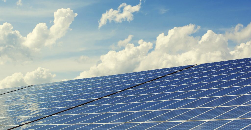 Solar-Panels-with-Sky-Background Solar panels angled towards the sky with bright blue, cloudy sky in background