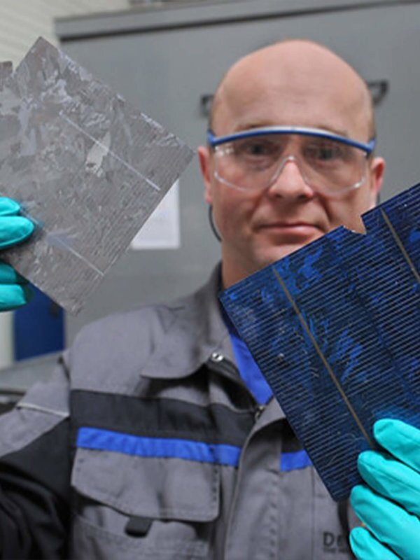 Bald, white, male with safety glasses and turquoise gloves holidng solar panel scraps